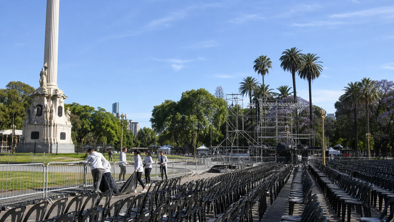 Preparativos con sillas y vallado en una plaza porteña junto a un monumento
