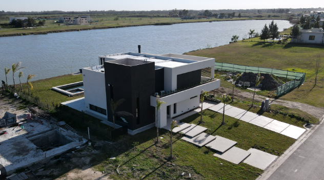 Obra activa de una vivienda en construcción dentro de un barrio privado del corredor norte bonaerense, con estructura de hormigón y cerco verde de seguridad