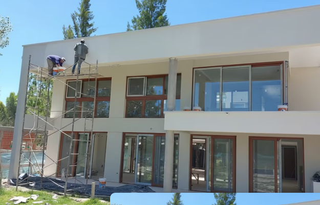 Trabajadores en la etapa de terminación exterior de una vivienda moderna en un barrio privado del corredor norte, con fachada blanca y carpintería de aluminio
