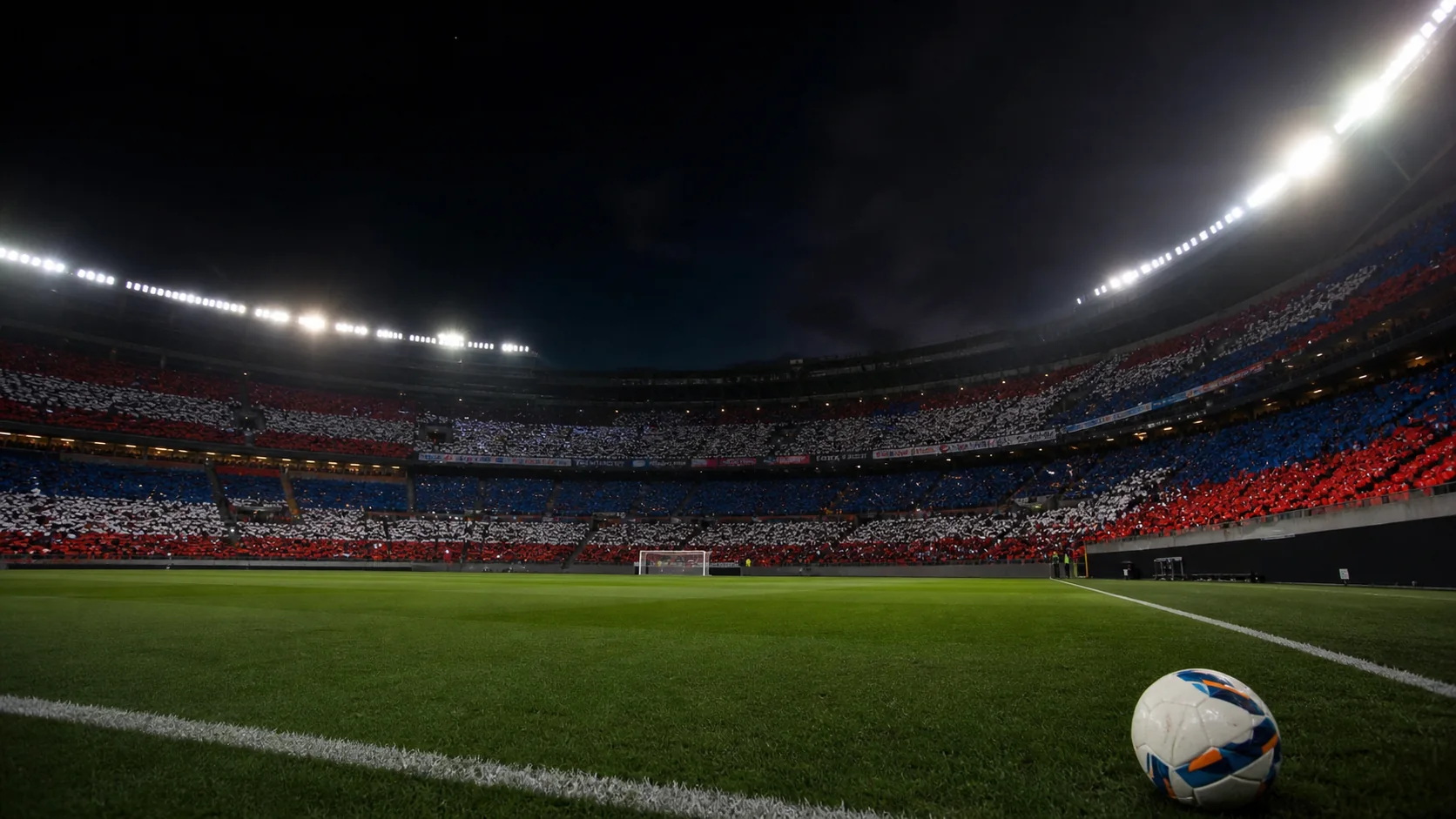 Estadio de fútbol iluminado de noche con una pelota junto a la línea lateral