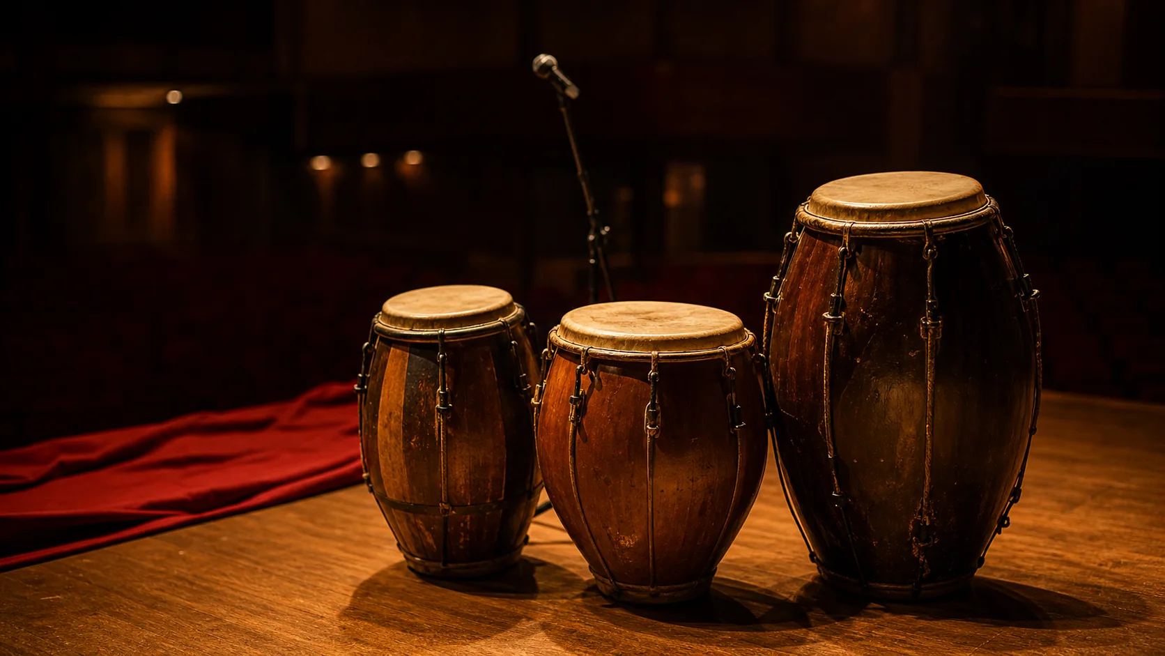 Tres tambores de candombe sobre un escenario vacío iluminado con luz cálida