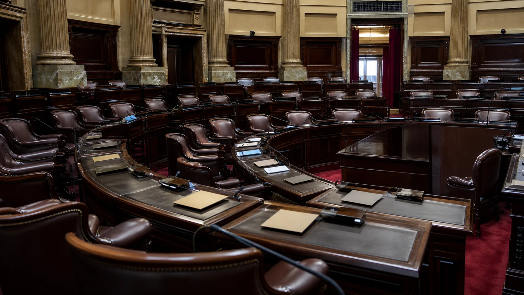 Recinto legislativo vacío con bancas curvas y carpetas sobre los escritorios